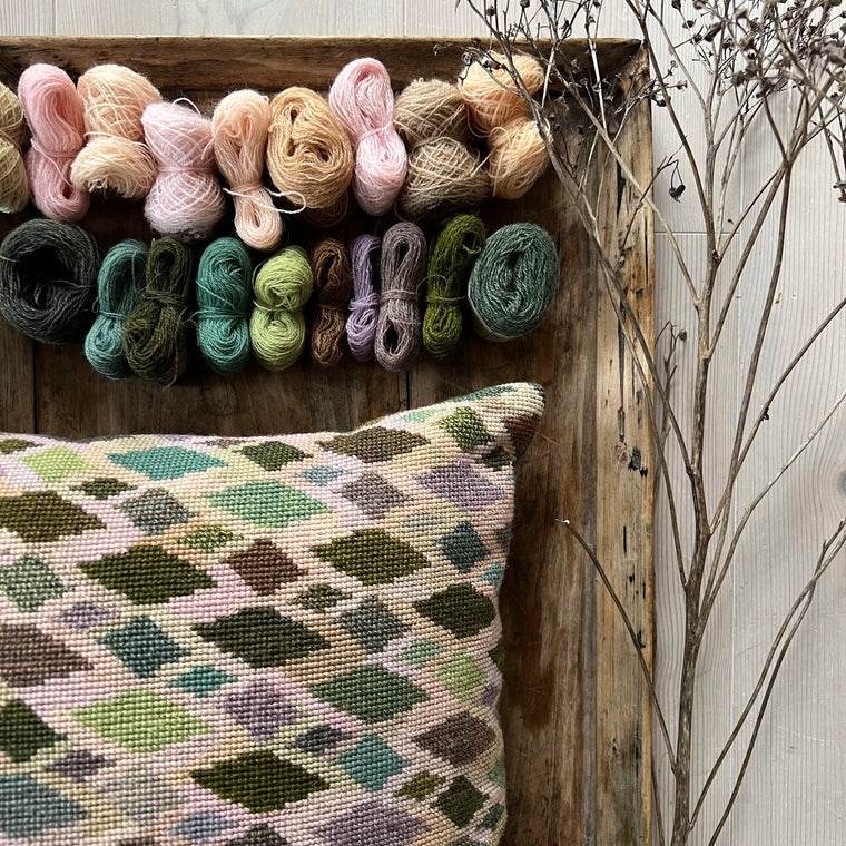 Cushion no2 pute ferdig brodert med garnnøster liggende på et rustikt trefat