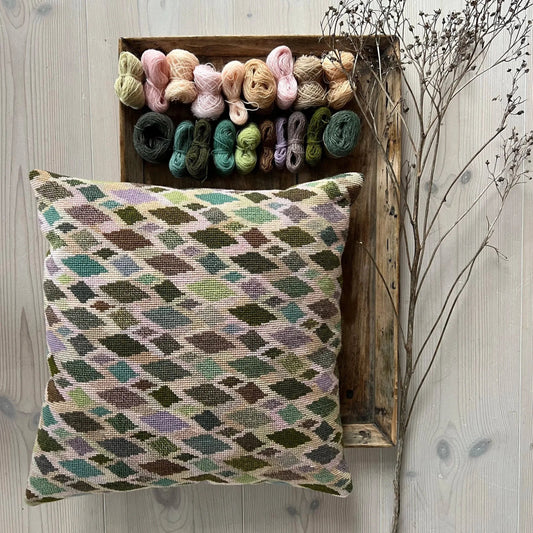 Cushion no2 pute ferdig brodert med garnnøster liggende på et rustikt trefat og tregulv