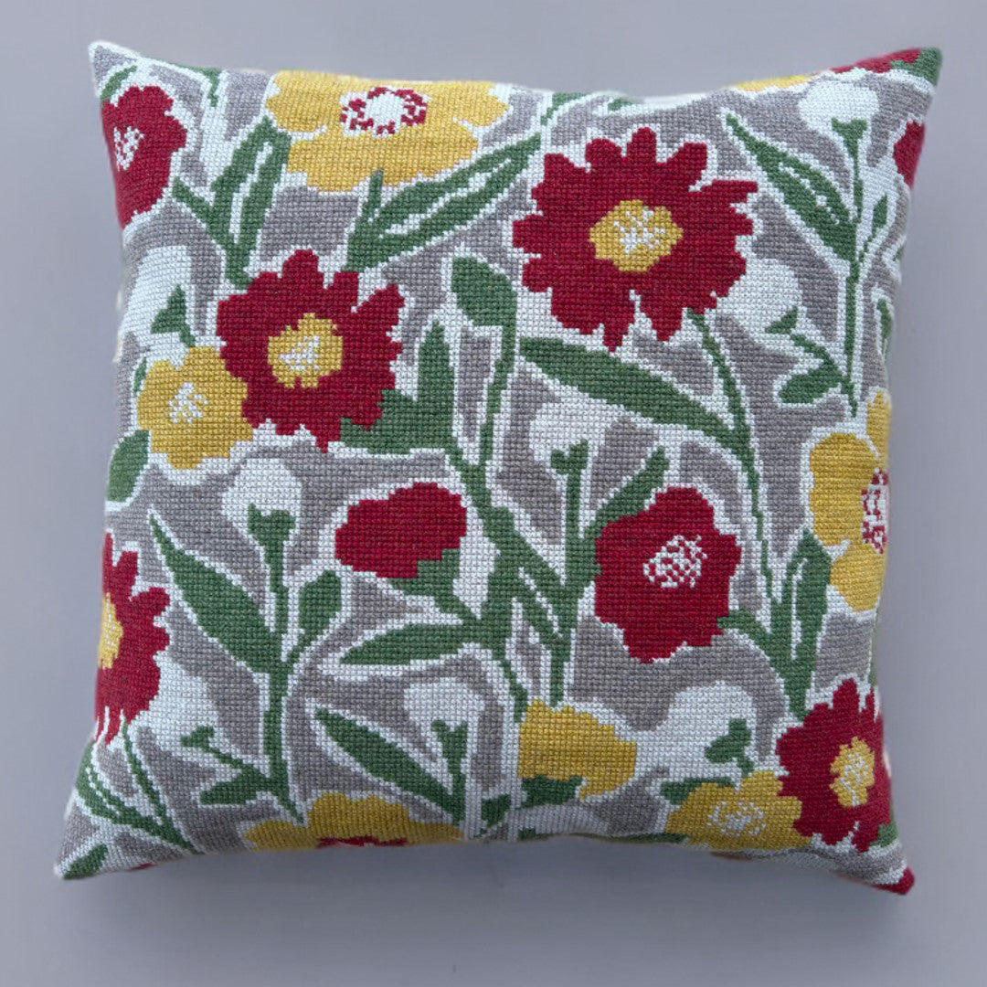 Brodert pute med blomster i fargene rød, gul, grønn og hvit.